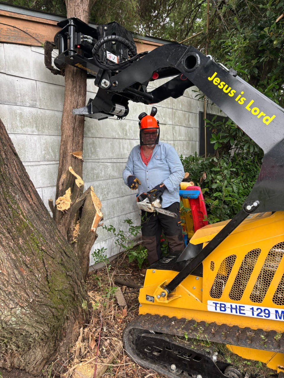 A chainsaw ministry volunteer clearing a tree beside a Lancaster home with a mini skid steer.