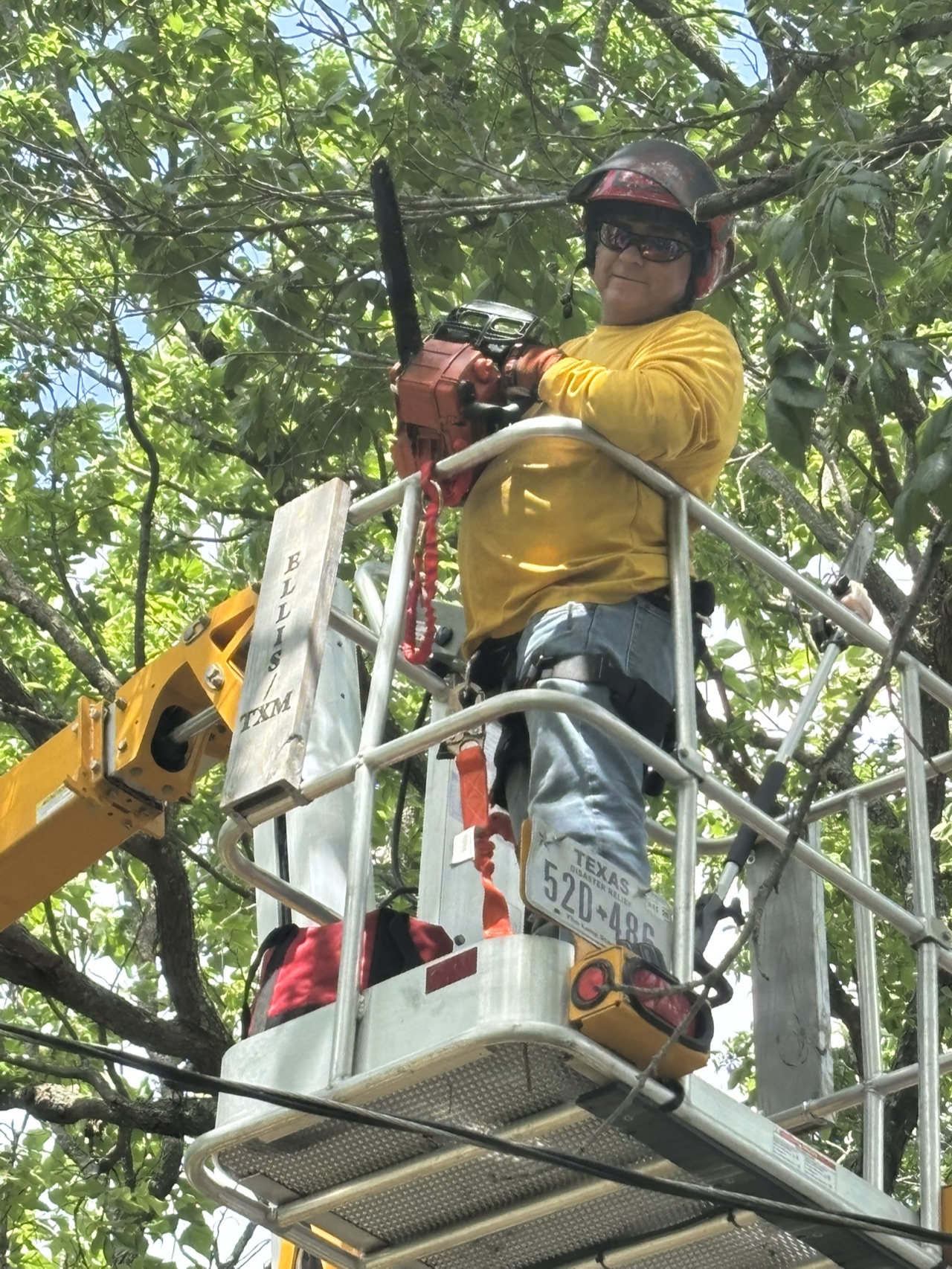 A chainsaw ministry volunteer cutting tree limbs from a lift during the Brooks community service project.