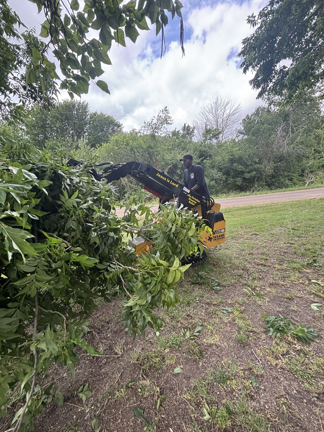 A Texans on Mission skid steer clearing branches near a roadside during the Brooks community service project.