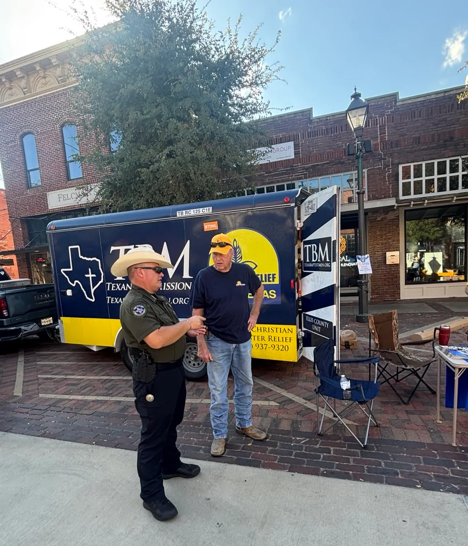 An ECDR volunteer speaking with a law enforcement representative beside the Ellis County disaster relief trailer.