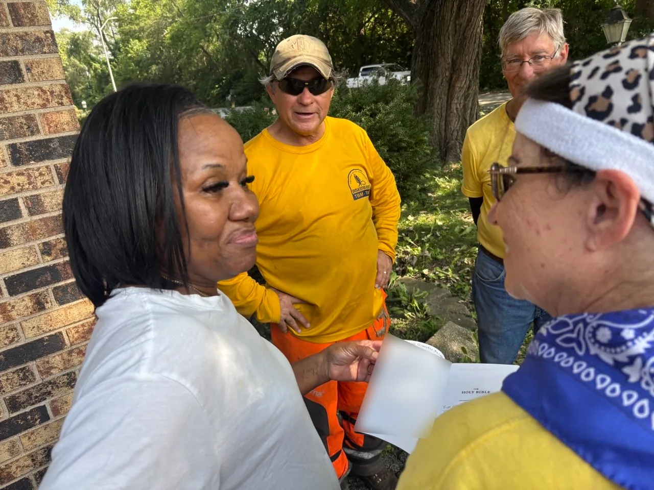 Glenwood homeowner receiving an open Bible from ECDR volunteers after storm cleanup work.