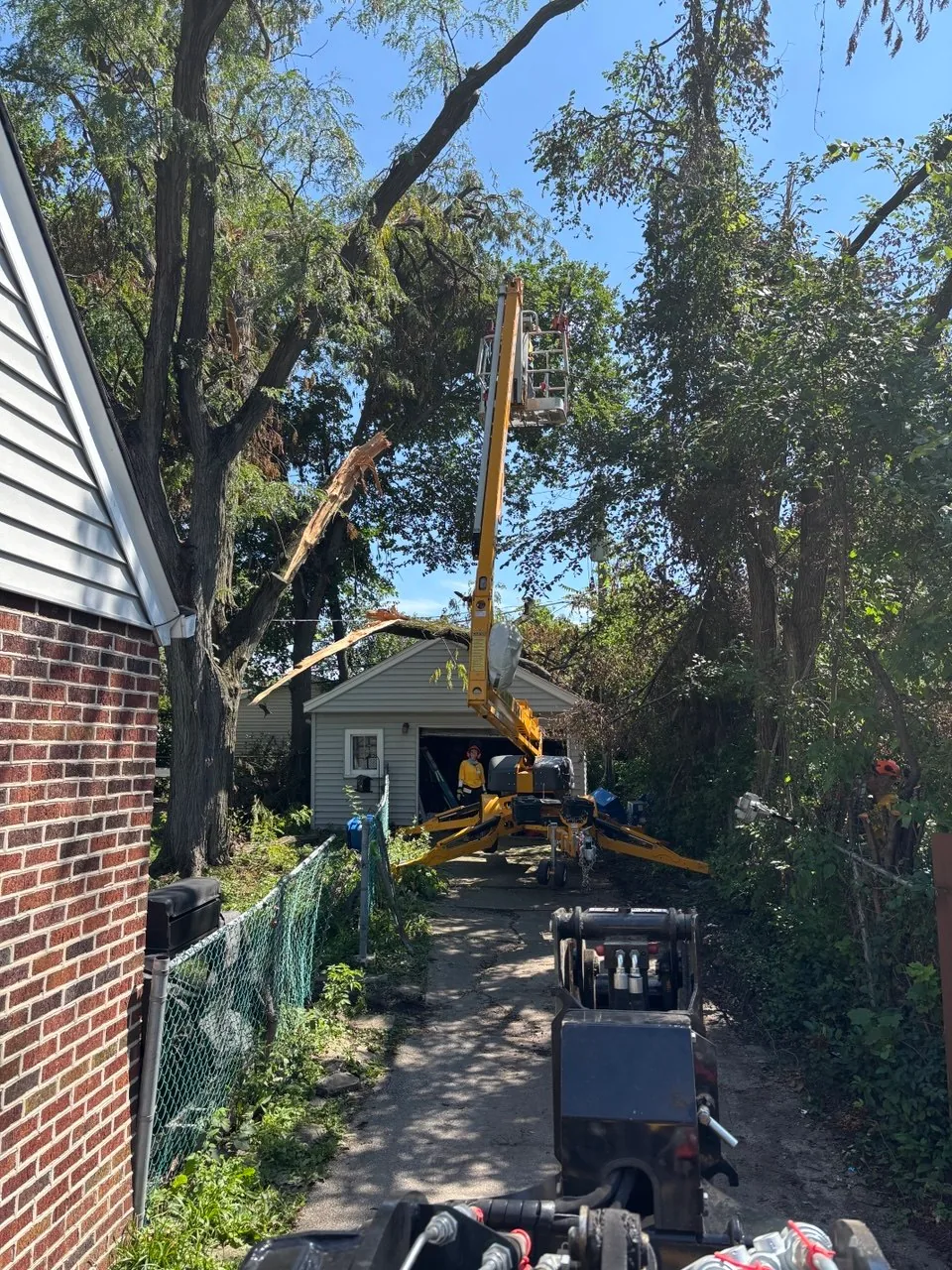 Bucket lift and chainsaw equipment positioned beside a Glenwood home for hazardous tree removal.