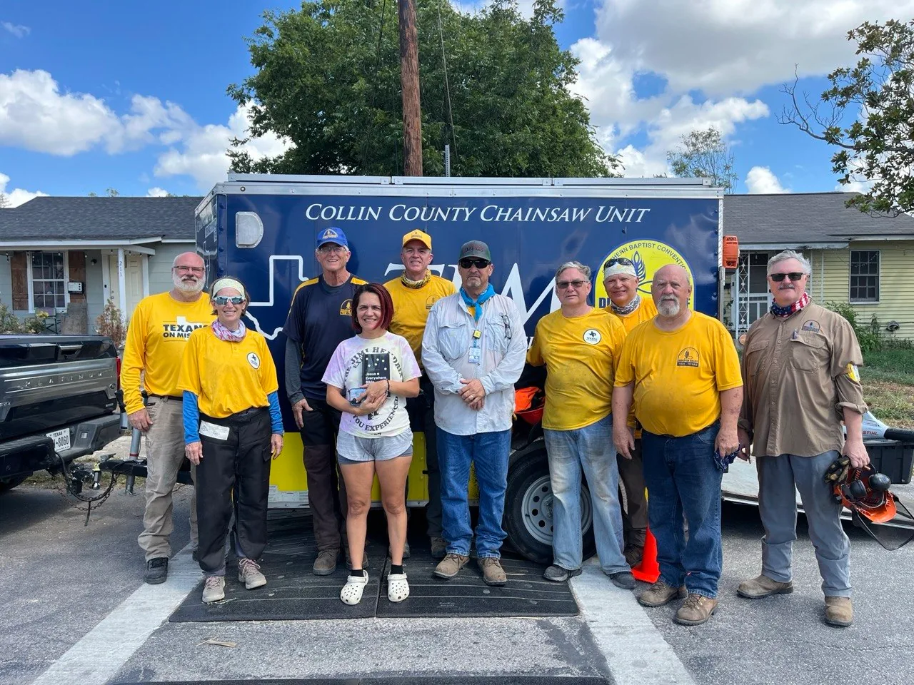 San Antonio homeowner standing with chainsaw ministry volunteers in front of the Collin County Chainsaw Unit trailer.